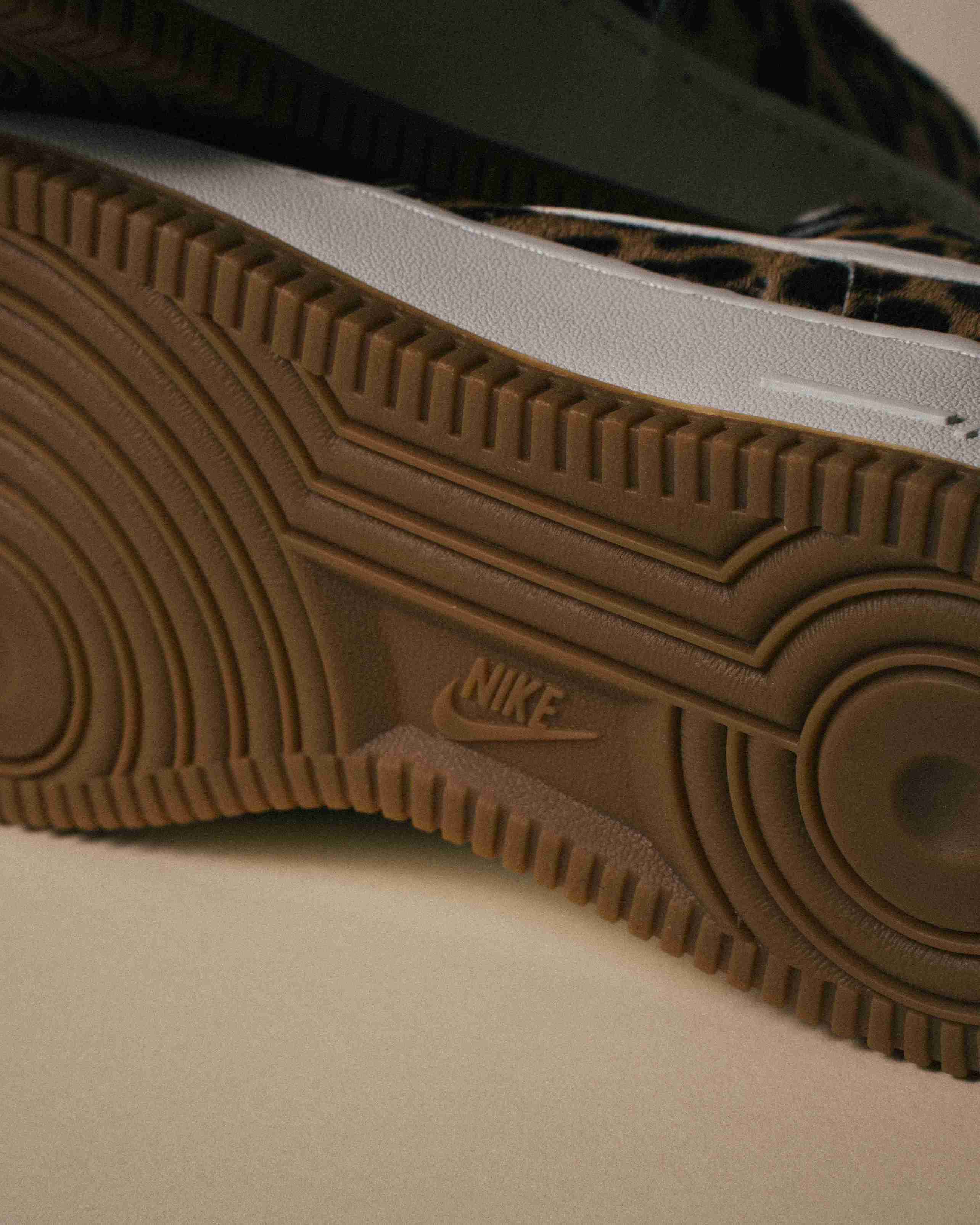 Paire de sneakers Nike Air Force 1 à motif léopard, placée à côté d’une boîte Nike grise sur un fond beige, vue artistique avec lumière douce.